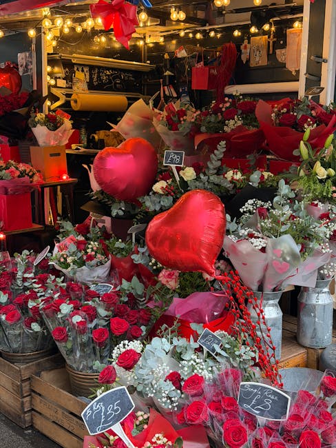 A vibrant display of floral arrangements at a florist shop, featuring an abundance of red roses, white flowers, and greenery, arranged in bouquets wrapped in clear and decorative paper. Two shiny red